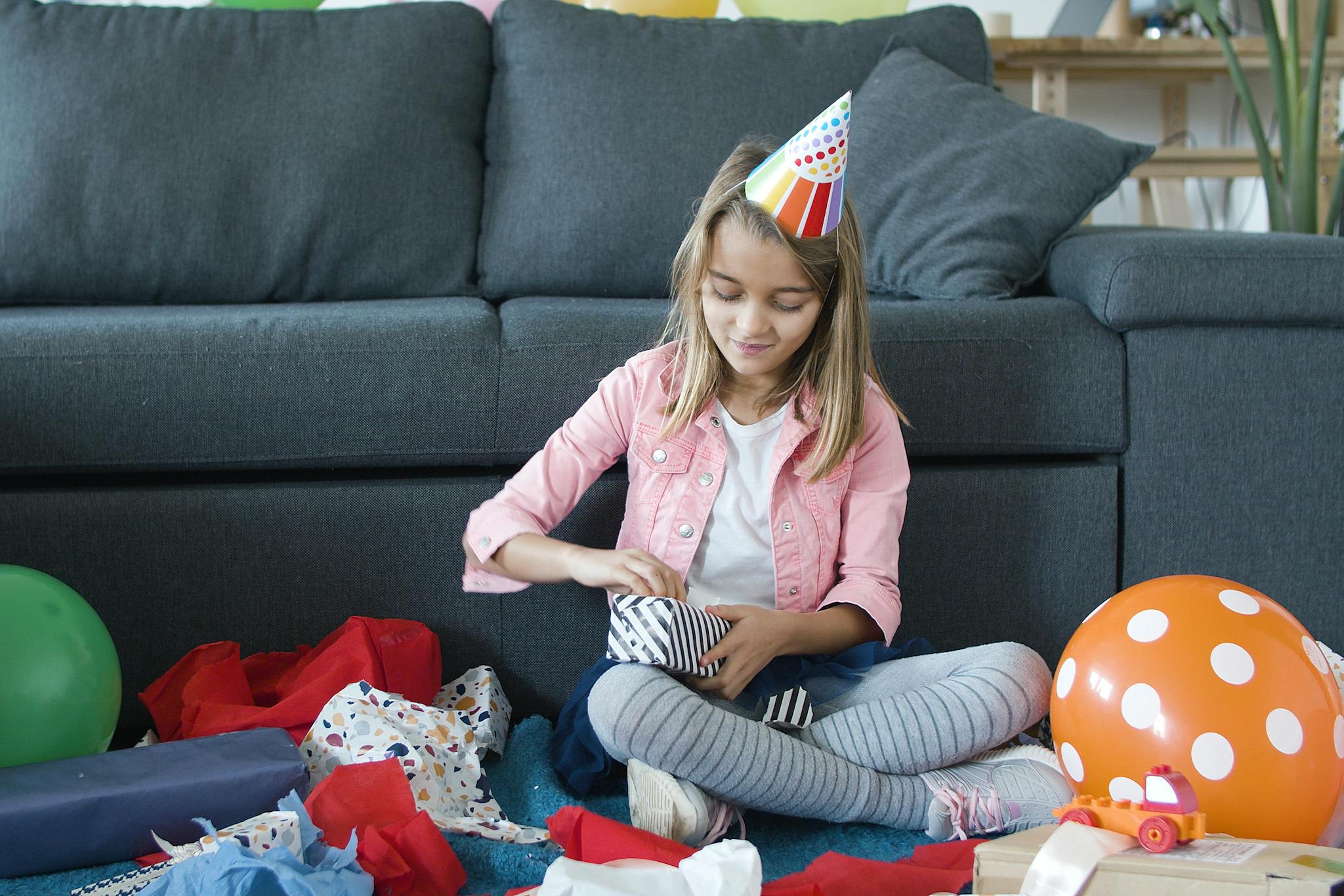 A girl in a party hat opens gifts in a vibrant and joyful indoor birthday setting.