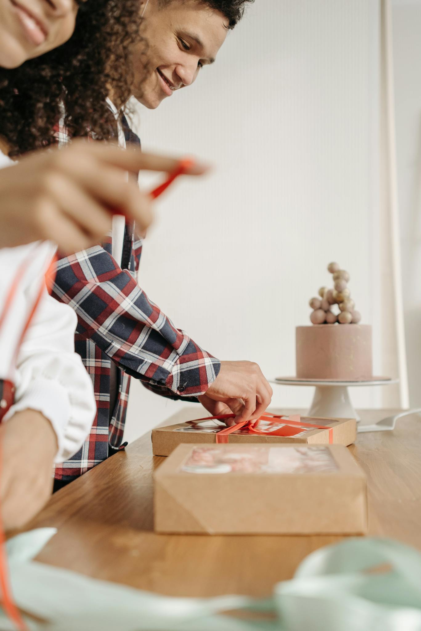 Two people happily wrapping gifts with a beautifully decorated cake in the background.